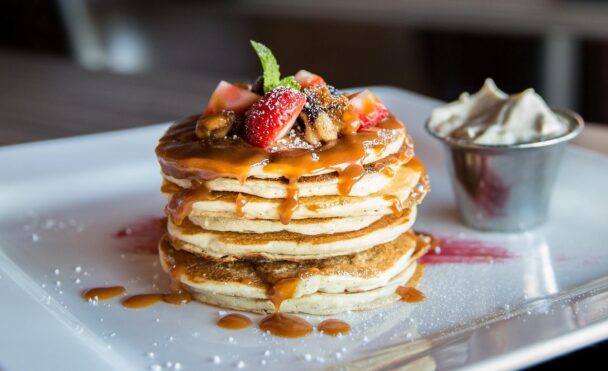 Stack of golden fluffy pancakes topped with butter and maple syrup on a white plate