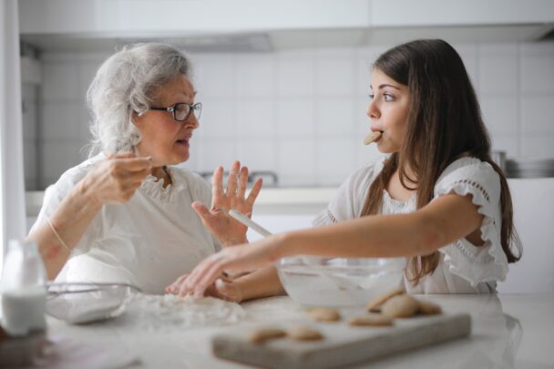 Elderly woman and young woman baking cookies together in a clean white kitchen, showing the joy of cooking with good kitchen habits.