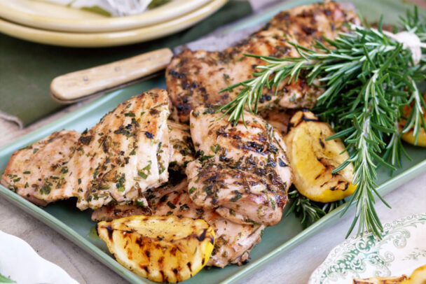 Juicy grilled chicken with rosemary served on a rustic wooden board with lemon and fresh herbs