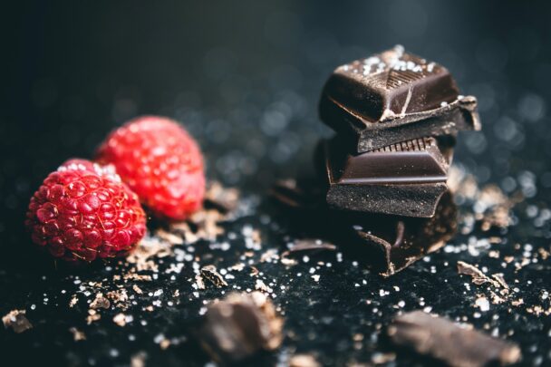 A close-up of rich, dark chocolate squares on a rustic table with cocoa beans. This Pin highlights the health benefits of dark chocolate, including its role in heart health, mood enhancement, and anti-aging.