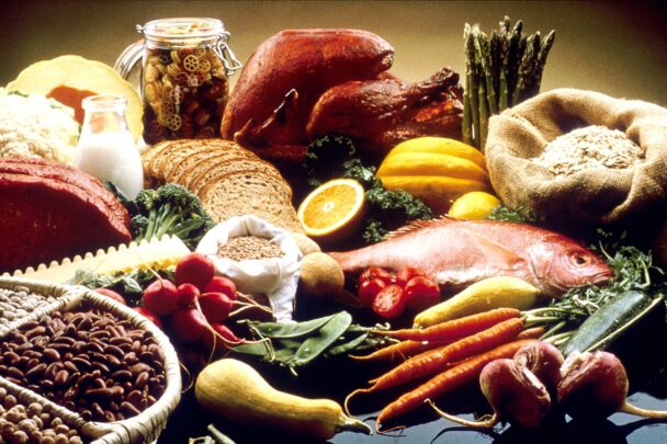 A colorful spread of iron-rich foods including leafy greens, whole grains, red meat, fish, legumes, root vegetables, and citrus fruits on a rustic table.