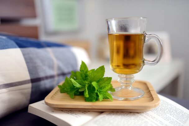 Flat lay of a steaming cup of green tea with lemon, surrounded by loose leaves and fresh herbs, representing the health benefits of green tea