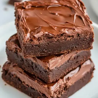 Stack of fudgy 3 ingredient Nutella brownies with a glossy chocolate top, displayed on a white plate