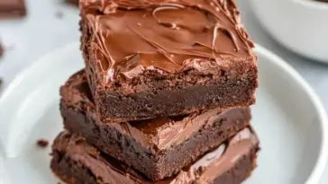 Close-up of stacked 3 ingredient Nutella brownies with glossy chocolate tops on a white plate