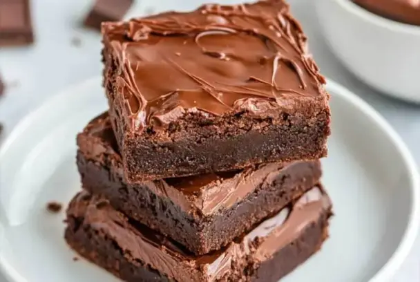 Close-up of stacked 3 ingredient Nutella brownies with glossy chocolate tops on a white plate