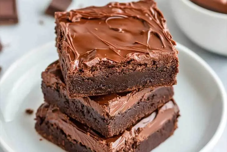 Close-up of stacked 3 ingredient Nutella brownies with glossy chocolate tops on a white plate