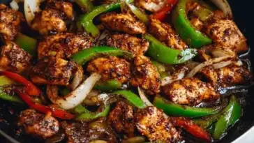 Close-up of stir-fried black pepper chicken with bell peppers and onions in a glossy pepper sauce, cooked in a skillet.