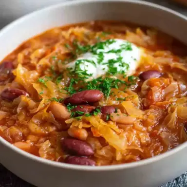 Bowl of traditional Croatian cabbage and beans stew (Zelje i Grah) with red and white beans, sauerkraut, and a dollop of sour cream topped with fresh parsley.