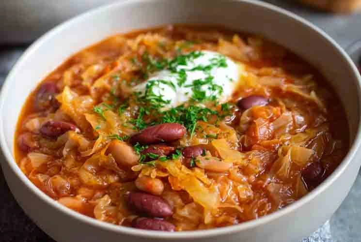 Close-up of a traditional Croatian cabbage and bean stew (Zelje i Grah) featuring red beans, sauerkraut, and sour cream, garnished with fresh parsley in a white bowl.