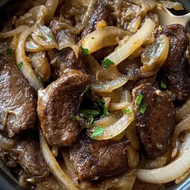 A close-up of beef liver and caramelized onions in a black bowl, garnished with fresh herbs – a classic and hearty comfort food dish.