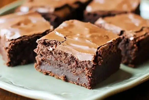 Close-up image of thick, chewy Lunch Lady Brownies with shiny chocolate frosting on a green plate, resembling vintage school cafeteria treats.