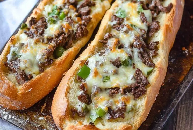 Freshly baked Philly Cheesesteak Bread on a tray, stuffed with juicy steak, cheese, and green bell peppers.