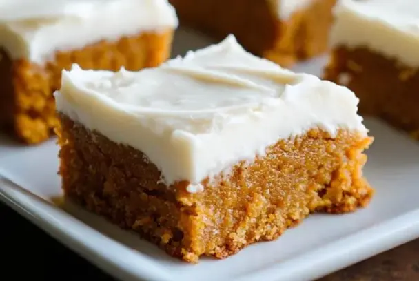 Soft pumpkin bar topped with creamy frosting on a white plate, a cozy and easy fall dessert