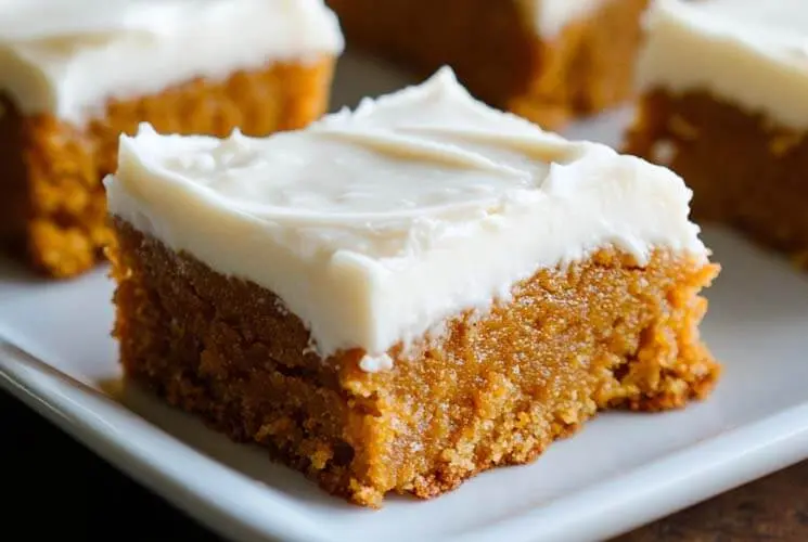 Soft pumpkin bar topped with creamy frosting on a white plate, a cozy and easy fall dessert