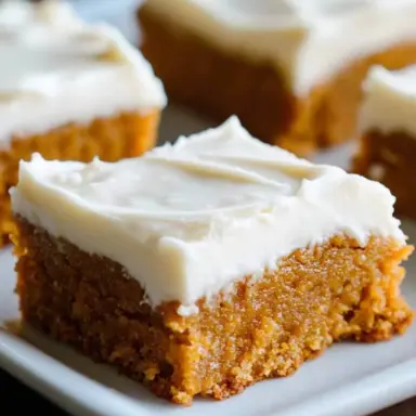 Close-up of a moist pumpkin bar topped with creamy white frosting on a plate, perfect fall dessert