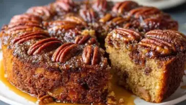 Whole pecan upside down cake on a white plate with one slice removed, showing a gooey caramel nut topping and moist golden cake.