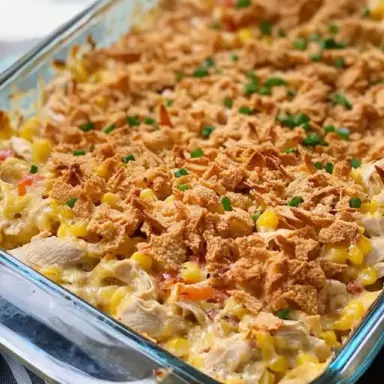 A baked casserole in a white dish filled with creamy chicken, melted cheese, pasta, and topped with a golden, crispy cracker crust – served with a side of green beans.