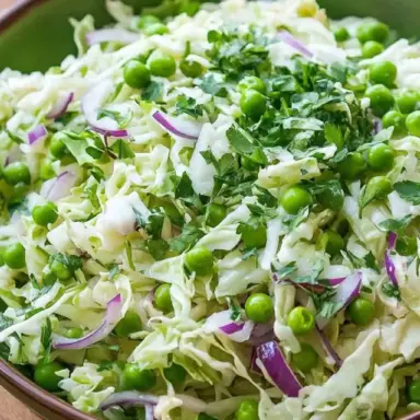A vibrant bowl of cabbage and pea salad with shredded green cabbage, sweet green peas, fresh herbs, and a light dressing, served in a white bowl on a rustic table — a perfect refreshing side dish for any season.