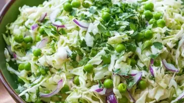Overhead shot of a vibrant cabbage and pea salad with shredded green cabbage, bright green peas, thinly sliced red onions, and fresh chopped parsley in a green bowl — a refreshing and healthy side dish idea.