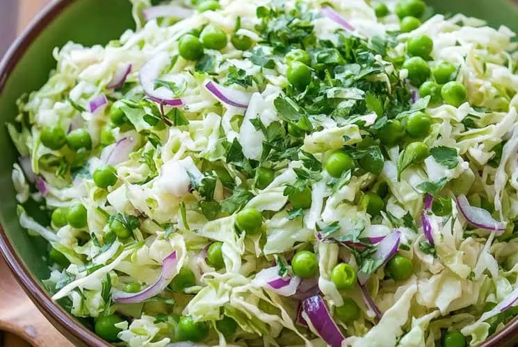 Overhead shot of a vibrant cabbage and pea salad with shredded green cabbage, bright green peas, thinly sliced red onions, and fresh chopped parsley in a green bowl — a refreshing and healthy side dish idea.