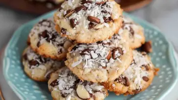 Plate of homemade 4 ingredient Almond Joy cookies with toasted coconut, melty chocolate chips, and crunchy almonds on top.