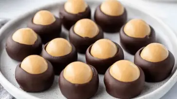 Plate of classic homemade buckeye candies featuring smooth peanut butter centers partially dipped in chocolate. Easy, no-bake holiday dessert idea.