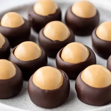Close-up of no-bake buckeye candies—creamy peanut butter balls partially dipped in chocolate, arranged neatly on a plate. Classic Ohio holiday treat.
