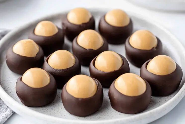 Plate of classic homemade buckeye candies featuring smooth peanut butter centers partially dipped in chocolate. Easy, no-bake holiday dessert idea.