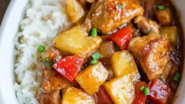 Close-up of Slow Cooker Hawaiian Pineapple Chicken served with rice, featuring tender chicken pieces, sweet pineapple chunks, red bell peppers, and savory sauce.