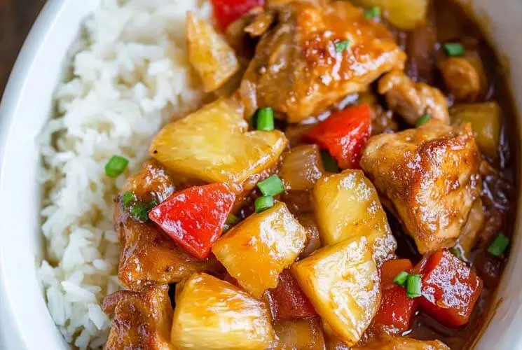 Close-up of Slow Cooker Hawaiian Pineapple Chicken served with rice, featuring tender chicken pieces, sweet pineapple chunks, red bell peppers, and savory sauce.