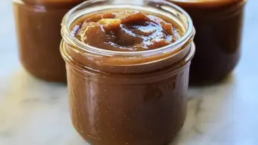 Close-up of rich, spiced homemade apple butter in glass jars, ideal for spreading on toast or packaging as fall gifts