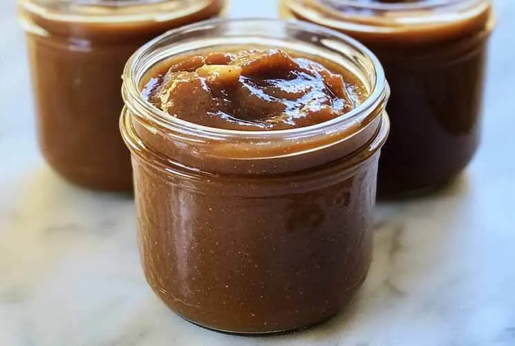 Close-up of rich, spiced homemade apple butter in glass jars, ideal for spreading on toast or packaging as fall gifts