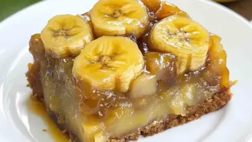 A close-up of a slice of banana upside down cake with thick caramelized banana rounds on top and a moist, glossy interior, served on a white plate.
