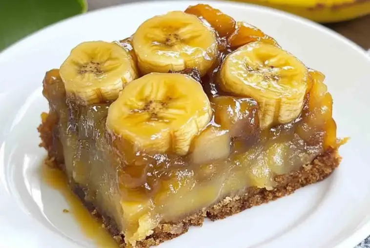 A close-up of a slice of banana upside down cake with thick caramelized banana rounds on top and a moist, glossy interior, served on a white plate.