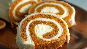 Sliced carrot cake roll with a creamy spiral of cream cheese filling, served on a wooden plate and ready to enjoy.