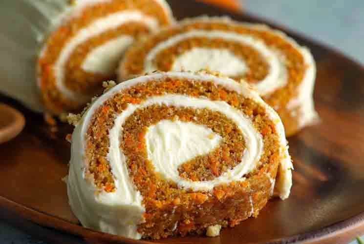 Sliced carrot cake roll with a creamy spiral of cream cheese filling, served on a wooden plate and ready to enjoy.