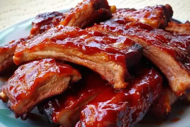 Glazed Coca Cola BBQ ribs piled on a plate, showcasing their tender texture and shiny, caramelized barbecue sauce