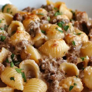 Close-up of creamy beef and pasta shells in a white bowl, topped with melted cheese and garnished with fresh parsley—rich, comforting, and cheesy.