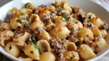 Creamy beef and shell pasta served in a white bowl, topped with melted cheese and garnished with fresh parsley—a rich and comforting homemade meal.