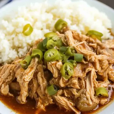 Close-up of shredded Crock Pot Mississippi Chicken topped with sliced pepperoncini, served with white rice on a plate