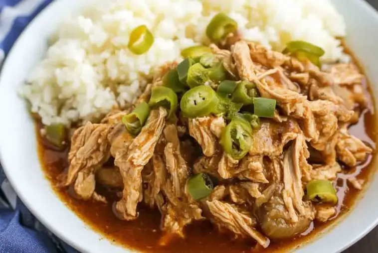 Plate of shredded Crock Pot Mississippi Chicken topped with sliced pepperoncini peppers, served with white rice and rich, savory sauce