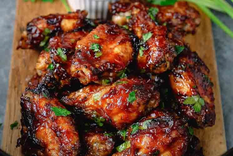 Sticky Crockpot BBQ chicken wings served on a wooden board, garnished with chopped parsley and paired with a side of barbecue sauce.