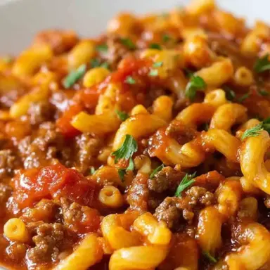 Close-up of a bowl of easy American goulash with elbow macaroni, ground beef, and tomato sauce, garnished with fresh parsley.