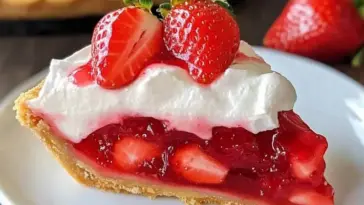 A slice of no-bake strawberry pie with a golden crust, glossy red strawberry filling, fluffy whipped cream, and fresh strawberries on top.
