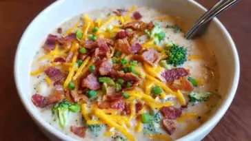 Creamy loaded broccoli and potato soup topped with melted cheddar, bacon pieces, and fresh chopped green onions in a white bowl with spoon.
