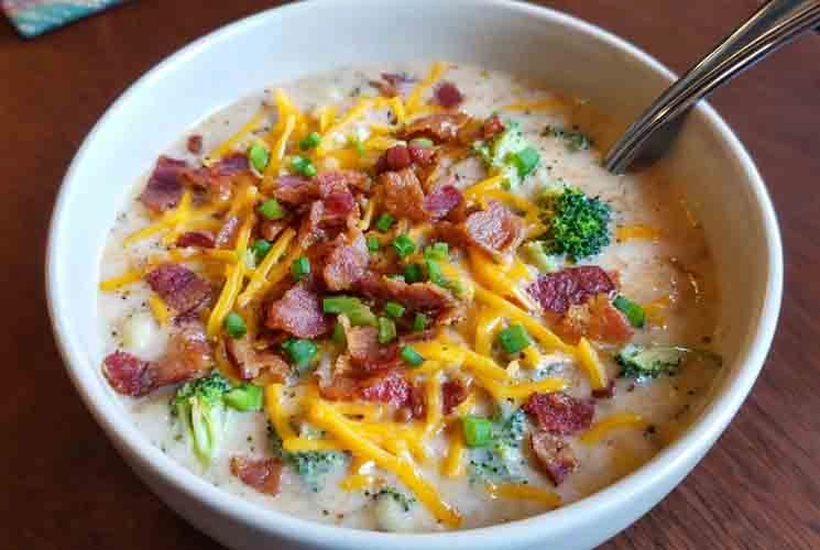 Creamy loaded broccoli and potato soup topped with melted cheddar, bacon pieces, and fresh chopped green onions in a white bowl with spoon.