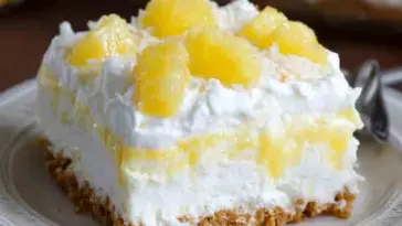 Close-up of a slice of no bake pineapple dream dessert with layers of whipped cream, crushed pineapple, and graham cracker crust, served on a plate.