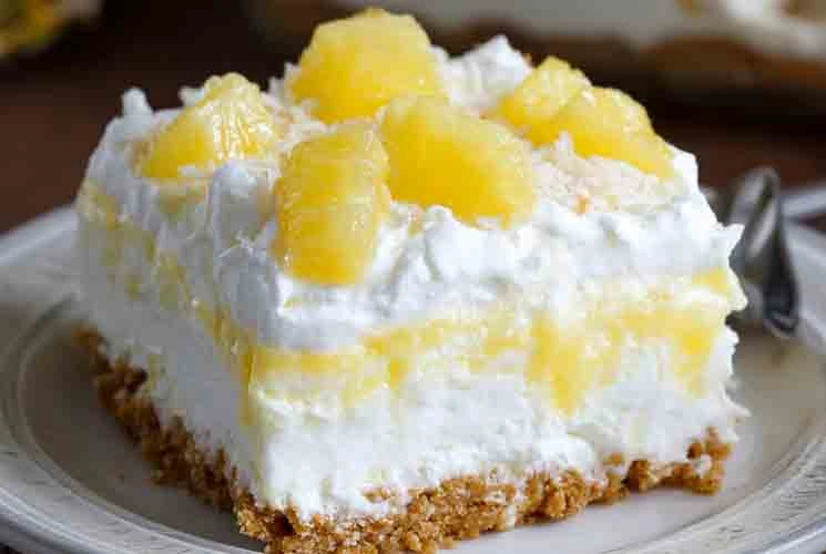 Close-up of a slice of no bake pineapple dream dessert with layers of whipped cream, crushed pineapple, and graham cracker crust, served on a plate.