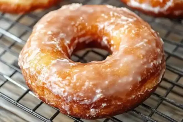 Freshly glazed old fashioned sour cream donut with crackled glaze on a wire cooling rack.