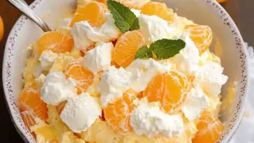 Overhead shot of Orange Creamsicle Salad in a white bowl, topped with whipped cream, mandarin orange slices, and fresh mint leaves.
